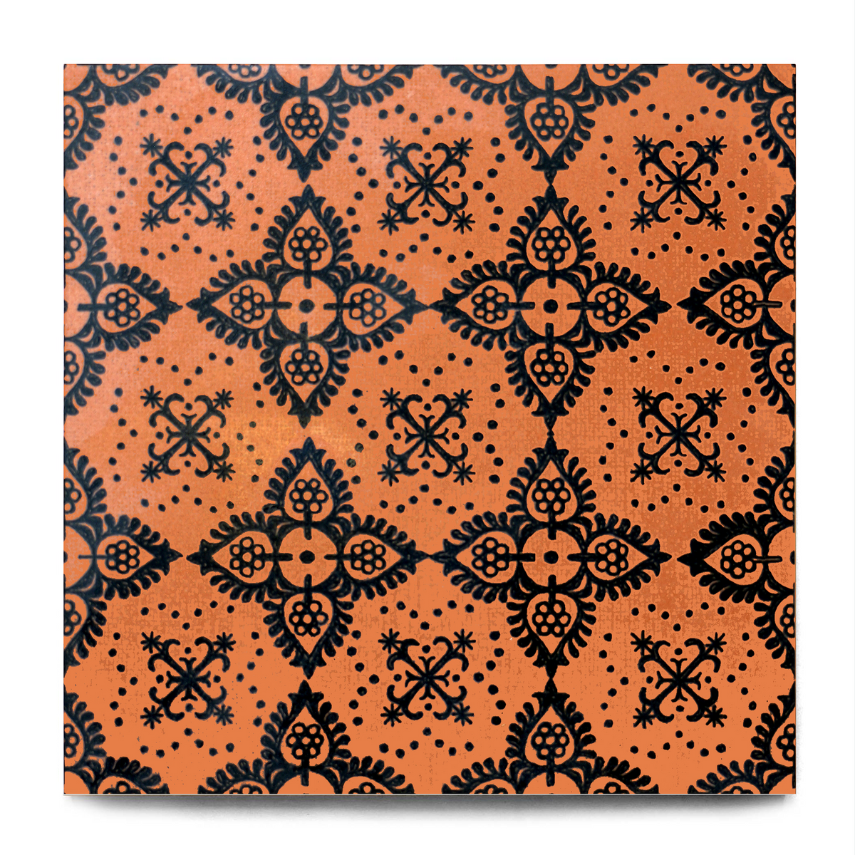A square decorative tile featuring a repeating black ornamental damask-style pattern on a warm orange background, shown against a light gray backdrop with a subtle drop shadow.